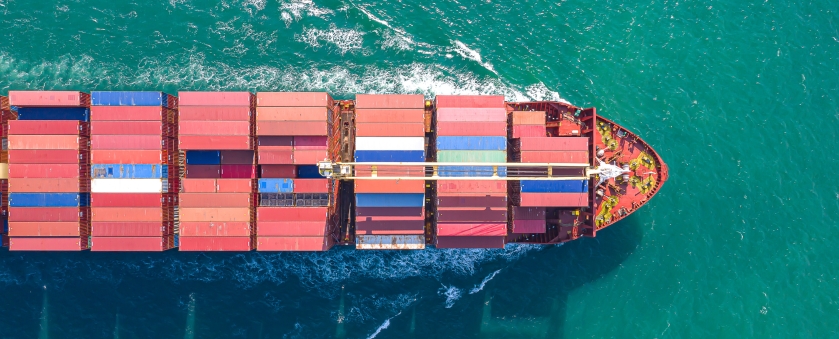 Aerial view of a large red and blue container ship sailing on clear water, symbolising the supply chain's transport and logistics services.