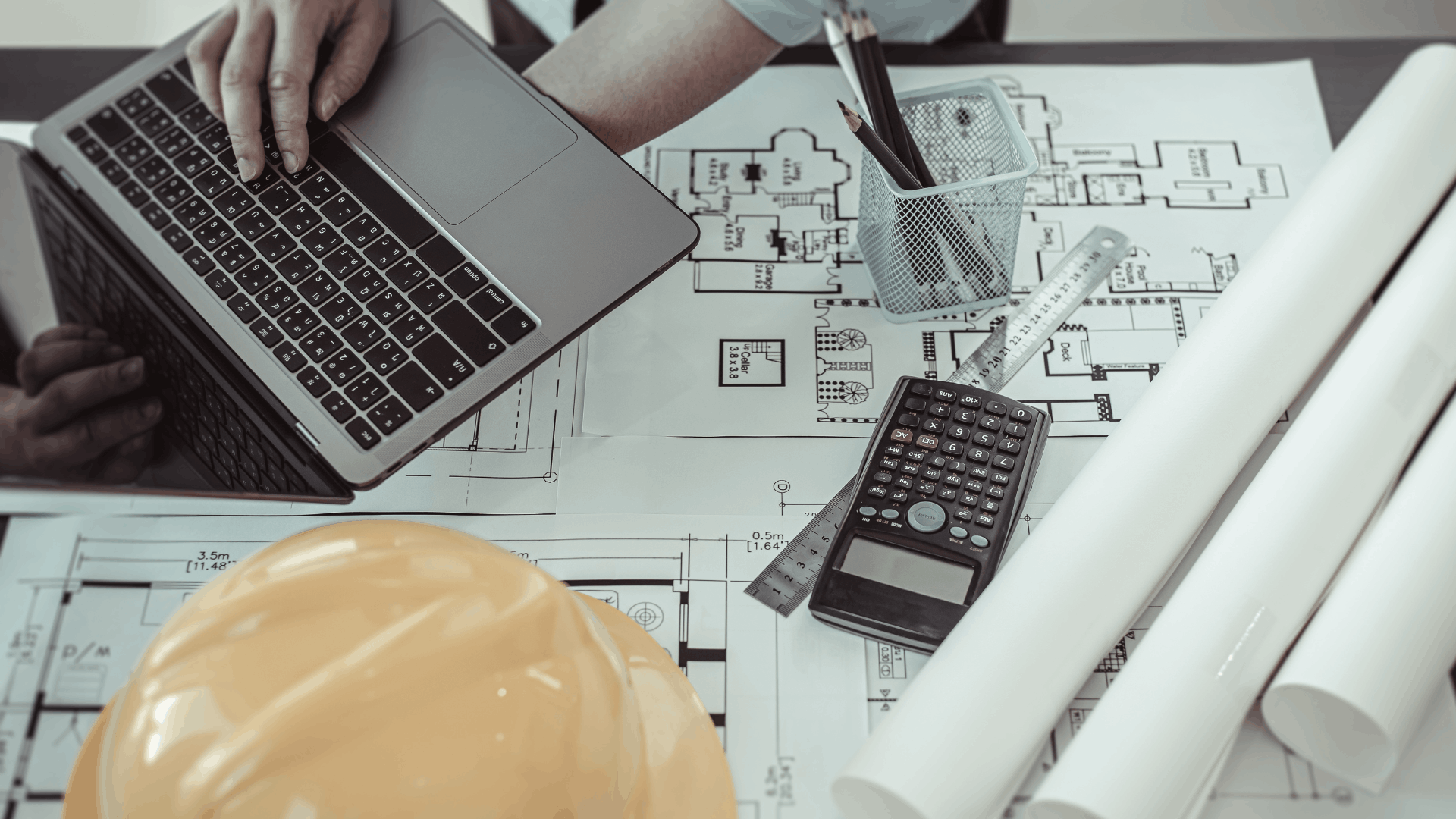 Laptop posé sur des plans techniques avec casque de chantier et calculatrice — illustration d'un projet ERP dans le secteur de l'ingénierie