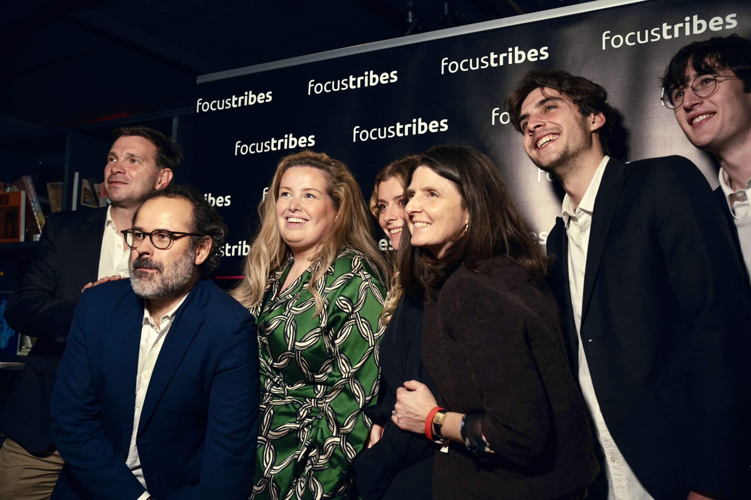 Photo d'équipe souriante devant un fond de marque Focustribes lors d'un événement, montrant un esprit de collaboration et de convivialité