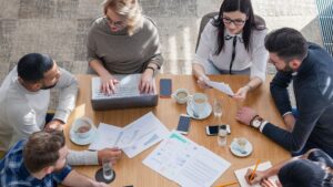Groupe de professionnels en réunion autour d’un bureau, analysant des documents financiers et des graphiques avec un ordinateur portable.
