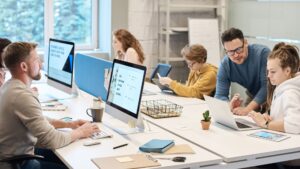 Équipe de travail en open space, collaborant sur des projets avec ordinateurs, tablettes et documents dans un environnement moderne.
