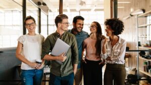 Groupe de jeunes professionnels souriants dans un bureau moderne, partageant un moment convivial après une réunion.