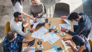 Équipe en réunion analysant des documents et des graphiques autour d’une table, échangeant des idées pour un projet collaboratif.