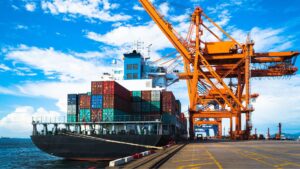 Navire porte-conteneurs en cours de déchargement dans un port logistique, avec grues industrielles et conteneurs colorés.