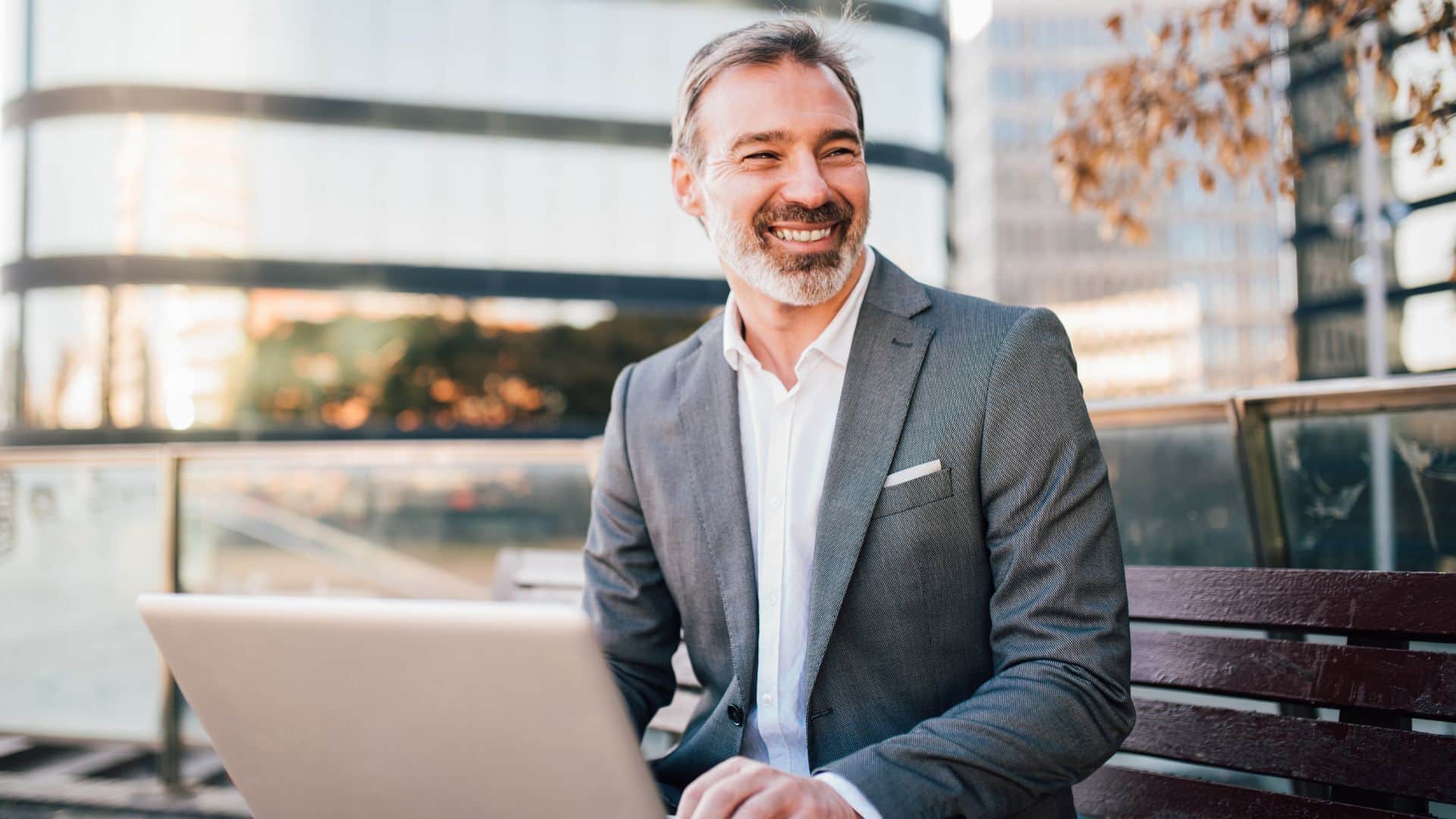 Consultant en affaires souriant, travaillant sur son ordinateur portable en extérieur dans un cadre urbain moderne.