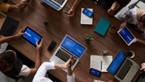 Consultants en réunion autour d’une table, analysant des données et des présentations sur tablettes, ordinateurs et smartphones.