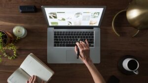 Vue aérienne d'un bureau avec un ordinateur portable, un carnet, une tasse de café et une main naviguant sur un site web d'images.