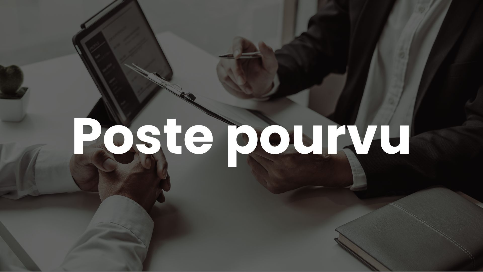 Entretien professionnel entre deux personnes en costume, avec une tablette, un carnet et un dossier sur un bureau blanc.