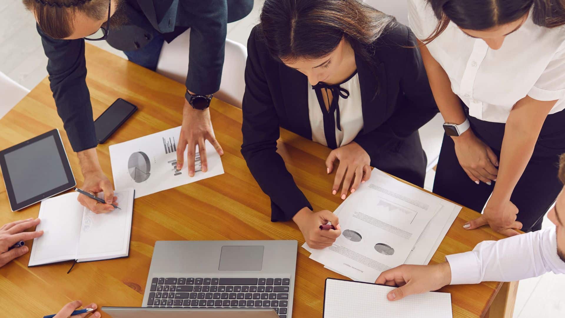 Groupe de professionnels analysant des graphiques et des données lors d'une réunion de travail autour d’un bureau en bois.